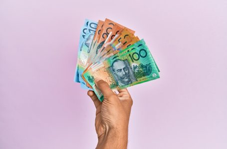 hand holding a fan of Australian bank notes against a pink background