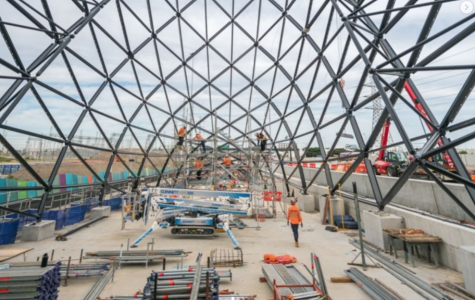 construction project in progress. A large steel framework towers over a worksite where workers wearing high vis go about their tasks.