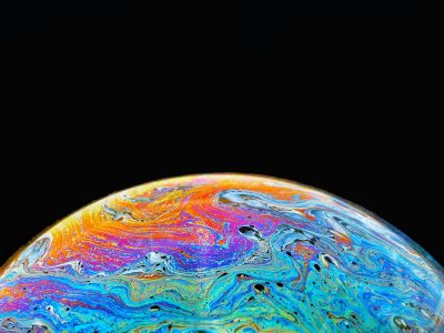 Close up of the surface of a bubble showing colours swirling on the surface, the background is black.